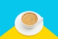 Black coffee with foam in a white cup on plate, at blue and yellow background Royalty Free Stock Photo