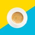 Black coffee with foam in a white cup on plate, top view, at blue and yellow background Royalty Free Stock Photo