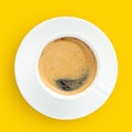 Black coffee with foam in a white cup on plate, top view, at yellow background Royalty Free Stock Photo