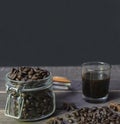 Black coffee in glass with roasted coffee beans in jar on rustic wooden table.Coffee dark background with copy space for text Royalty Free Stock Photo