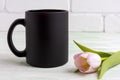 Black coffee mug mockup with gentle pink tulip Royalty Free Stock Photo