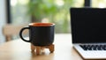 Black coffee mug with orange interior next to laptop workspace Royalty Free Stock Photo