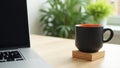 Black coffee mug with orange interior next to laptop workspace Royalty Free Stock Photo