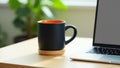 Black coffee mug with orange interior next to laptop workspace Royalty Free Stock Photo
