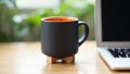 Black coffee mug with orange interior next to laptop workspace Royalty Free Stock Photo