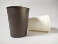 A black coffee paper cup and a laying white coffee paper cup on behind