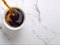 Black coffee pouring into white mug on white marble tabletop