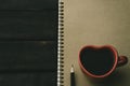 black coffee in a red heart shape coffee cup on a vintage notebook above dark grey wooden home office desk