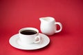 black coffee in small white coffee cup and milk jug on red background Royalty Free Stock Photo