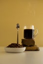 Black coffee with smoke in glass cup with coffee beans and vertical spoon, on the stones and table