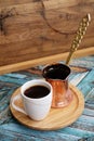 Black coffee in a white cup and copper cezve on round bamboo stand. Traditional turkish method