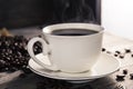 Black coffee in a white coffee cup with hot steam and coffee beans placed on a wooden table on a dark background. in a warm Royalty Free Stock Photo