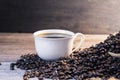 Black coffee in a white coffee cup with hot steam and coffee beans placed on a wooden table on a dark background. in a warm Royalty Free Stock Photo