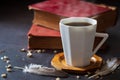 Black coffee in white cup and old books with feather and dried flower petals.