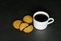 Black coffee in a white cup and some fresh tasty oat cookies on a black background