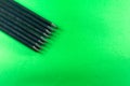 Black colored pencils in a row. Isolated on green background Royalty Free Stock Photo