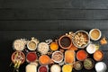 On a black colored wooden floor, various spices and beans are in bowls. Copy space, black background.