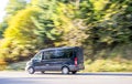 Black compact cargo business mini van running on the autumn road with trees on the side