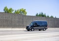 Black compact cargo mini van running on the road with concrete protection wall on the side Royalty Free Stock Photo