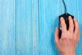 Black computer mouse with a hand on a blue wooden background with copy space for your text. Top view Royalty Free Stock Photo