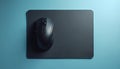 Black computer mouse rests on dark grey mousepad. Item sits on light blue flat surface. Minimalist tech accessory, ideal for Royalty Free Stock Photo