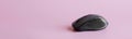 Black computer mouse with a scroll wheel, additional buttons and a rubber pad on a pink background. Copy space. Web banner