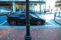 A black corvette in front of a red brick sidewalk with other parked cars on the street and a tall black lamp post in downtown