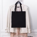 Black cotton eco tote bag on a hanger with elegant clothes, design mockup. Handmade shopping bags