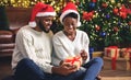 Black couple celebrating Christmas at home, unwrapping presents together