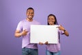 Black couple holding and pointing at blank white advertising placard Royalty Free Stock Photo