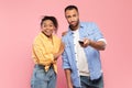 Black couple with remote control watching television program or show on TV over pink studio background Royalty Free Stock Photo