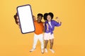 Black couple showing large mobile phone against yellow studio backdrop