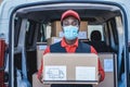 Black courier man delivering package in front of cargo truck wearing safety mask - Focus on face