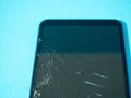 Black crashed smartphone with broken screen and body on a blue table in service.