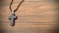 Black cross pendant on black rope, on wooden brown background. Royalty Free Stock Photo