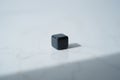 Single black cube on white marble surface with soft shadow, simple abstract geometric shape and object Royalty Free Stock Photo