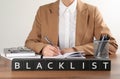 Black cubes with word Blacklist and woman working at wooden office desk, closeup Royalty Free Stock Photo