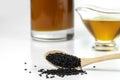 Black cumin seeds on a wooden spoon on a background of a glass gravy boat and of a bottle with black seed oil. Royalty Free Stock Photo