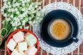 Black cup of coffee with milk on a saucer, marshmallow and bouquet of lily of the valley flowers on the table top view close up. Royalty Free Stock Photo