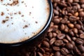 A black cup of black coffee with white foam close-up, stands on a table where coffee beans are scattered. top shot Royalty Free Stock Photo