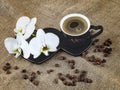 Black cup of coffee and white orchid flowers on a dark background. Coffee beans and burlap as decor. Romantic coffee composition. Royalty Free Stock Photo