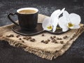 Black cup of coffee and white orchid flowers on a dark background. Coffee beans and burlap as decor. Royalty Free Stock Photo