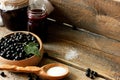 black currant berries in a wooden dish on a wooden table with a jar of jam, a wooden spoon with sugar, concatenation of