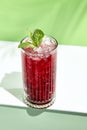 Black currant lemonade drink over green background. White table with sunlight and palm leaf hard shadow. Summer, tropical and Royalty Free Stock Photo