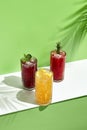 Black currant, orange and raspberry lemonade drink over green background. White table with sunlight and palm leaf hard shadow. Royalty Free Stock Photo