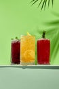 Black currant, orange and raspberry lemonade drink over green background. White table with sunlight and palm leaf hard shadow. Royalty Free Stock Photo