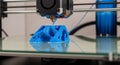 A black 3D printer with red laser beam printing a smooth blue cube object on glass table in workshop Royalty Free Stock Photo