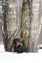 Black dachshund and shotgun near the birch tree in winter forest