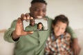 Black daddy and little son with smartphone making selfies indoor