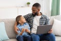 Black Daddy And Son Using Laptop And Phone At Home